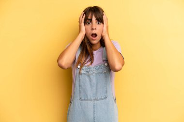 İspanyol güzel kadın hoş olmayan bir şekilde şok olmuş, korkmuş ya da endişeli görünüyor, ağzı sonuna kadar açık ve iki kulağını da elleriyle kapatıyor.