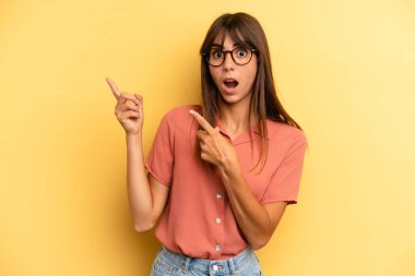 Hispanik güzel kadın neşeli ve şaşırmış hissediyor, şok olmuş bir ifadeyle gülümsüyor ve bir tarafı işaret ediyor.