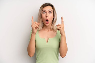 Genç sarışın kadın şaşırmış, şaşırmış ve ağzı açık görünüyor. İki elini de havaya kaldırıp boşluğu dolduruyor.