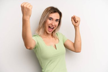 young adult blonde woman shouting triumphantly, looking like excited, happy and surprised winner, celebrating