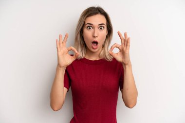 young adult blonde woman feeling shocked, amazed and surprised, showing approval making okay sign with both hands