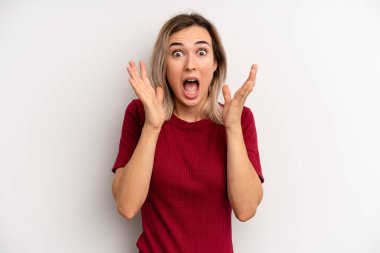 young adult blonde woman feeling shocked and excited, laughing, amazed and happy because of an unexpected surprise