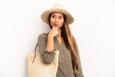 Asyalı genç kadın düşünüyor, kuşkulu ve şaşkın hissediyor. yaz ve şapka konsepti