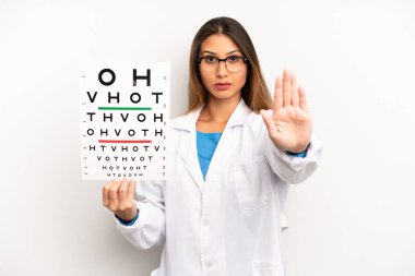 Asyalı genç kadın ciddi görünüyor. Avuç içini gösteriyor. Durdurma hareketi yapıyor. optik görüş testi konsepti