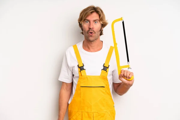 Adult Blond Man Looking Very Shocked Surprised Handyman Saw Concept — Stockfoto