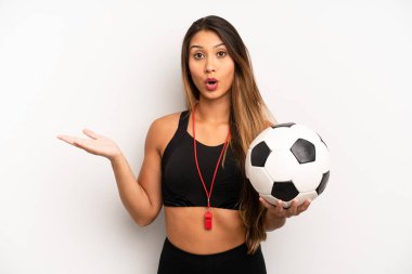 Asyalı genç kadın şaşırmış ve şok olmuş görünüyor. Çenesi düşmüş ve elinde bir nesne var. futbol ve fitness konsepti