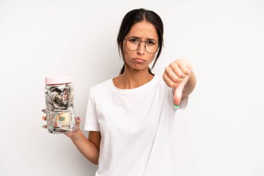 Latin kökenli güzel bir kadın kızmış, baş parmağını kaldırmış. domuz kumbarası tasarruf kavramı