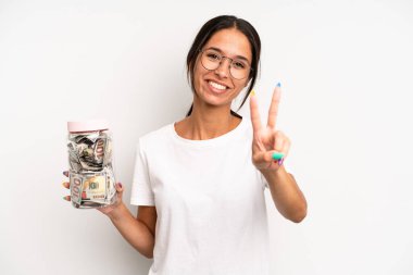 İspanyol güzel kadın gülümsüyor ve mutlu görünüyor, zafer ya da barış işareti yapıyor. domuz kumbarası tasarruf kavramı