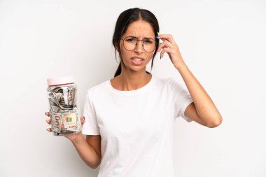 İspanyol güzel kadın kafası karışık ve şaşkın hissediyor, senin deli olduğunu gösteriyor. domuz kumbarası tasarruf kavramı