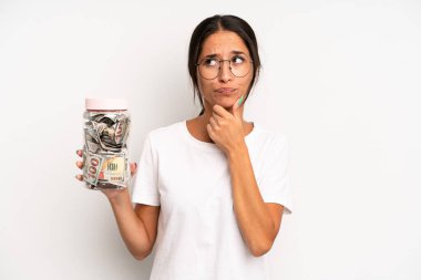 Hispanik güzel kadın düşünüyor, kuşkulu ve şaşkın hissediyor. domuz kumbarası tasarruf kavramı