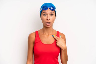 hispanic pretty woman looking shocked and surprised with mouth wide open, pointing to self. swimmer concept
