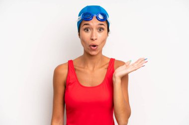 hispanic pretty woman looking surprised and shocked, with jaw dropped holding an object. swimmer concept