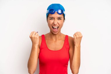 hispanic pretty woman shouting aggressively with an angry expression. swimmer concept