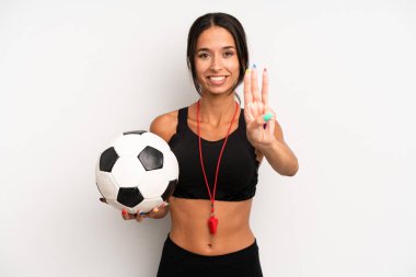İspanyol güzel kadın gülümsüyor ve arkadaş canlısı görünüyor, üç numarayı gösteriyor. futbol ve fitness konsepti