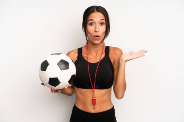 İspanyol güzel kadın şaşırmış ve şok olmuş görünüyor. Çenesi düşmüş ve elinde bir nesne var. futbol ve fitness konsepti