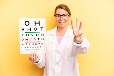 pretty blonde young woman smiling and looking friendly, showing number three. optical vision test concept