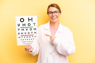 pretty blonde young woman smiling cheerfully, feeling happy and pointing to the side. optical vision test concept