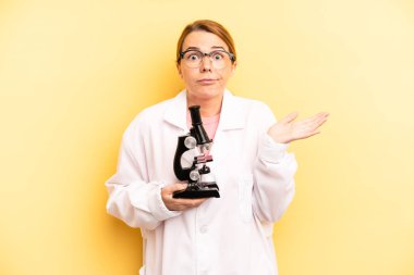 pretty blonde young woman feeling puzzled and confused and doubting. scients student with a microscope concept