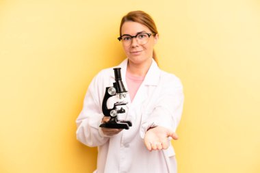 pretty blonde young woman smiling happily with friendly and  offering and showing a concept. scients student with a microscope concept