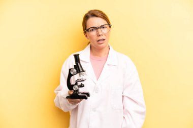pretty blonde young woman feeling puzzled and confused. scients student with a microscope concept