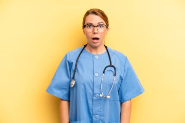 pretty blonde young woman looking very shocked or surprised. physician or doctor student concept