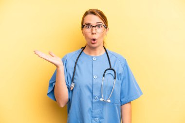 pretty blonde young woman looking surprised and shocked, with jaw dropped holding an object. physician or doctor student concept