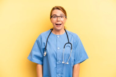 pretty blonde young woman looking happy and pleasantly surprised. physician or doctor student concept