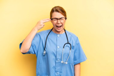 pretty blonde young woman looking unhappy and stressed, suicide gesture making gun sign. physician or doctor student concept