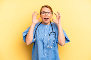 pretty blonde young woman screaming with hands up in the air. physician or doctor student concept