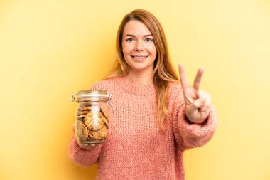 pretty blonde young woman smiling and looking friendly, showing number two. home made cookies concept