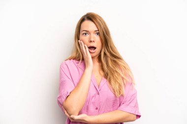 Sarışın, güzel bir kadın şok ve inanmazlık içinde, elleri yanağında ve kolları çaprazlanmış, sersemlemiş ve şaşırmış hissediyor.