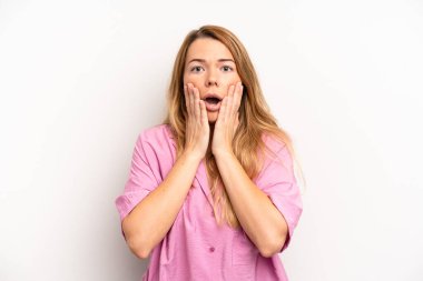 Sarışın, güzel bir kadın şok olmuş ve korkmuş hissediyor, ağzı açık ve elleri yanaklarında korkmuş görünüyor.