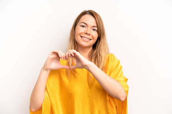 блондинка красивая женщина улыбается и чувствует себя счастливым, милый, романтичный и в любви, делая форму сердца с обеих рук