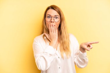 Sarışın, güzel bir kadın kendini mutlu, şaşkın ve şaşırmış hissediyor. Ağzını eliyle kapatıyor ve yanal kopya alanını işaret ediyor.