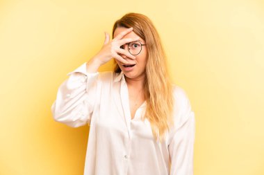 Sarışın, güzel bir kadın. Şok olmuş, korkmuş ya da korkmuş görünüyor. Yüzü elle kaplanmış ve parmaklarının arasından gizlice bakıyor.