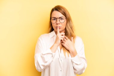 Sarışın, güzel bir kadın ciddi görünüyor ve parmaklarını dudaklarına bastırıp sessizlik ya da sessizlik talep ediyor, sır saklıyor.