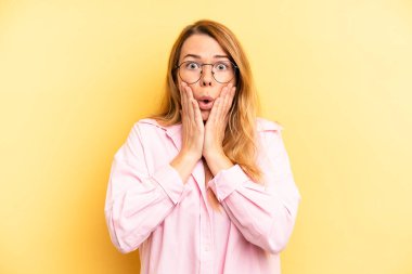 Sarışın, güzel bir kadın şok olmuş ve korkmuş hissediyor, ağzı açık ve elleri yanaklarında korkmuş görünüyor.