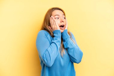 Sarışın, güzel bir kadın mutlu, heyecanlı ve şaşırmış hissediyor, iki eli yüzü yana bakıyor.