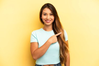 Asyalı güzel bir kadın neşeyle gülümsüyor, mutlu hissediyor ve yan ve yukarı doğru işaret ediyor, kopya uzayda nesne gösteriyor