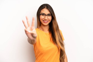 Asyalı güzel bir kadın gülümsüyor ve arkadaş canlısı görünüyor, üç ya da üç numarayı gösteriyor, eli önde, geriye doğru sayıyor.