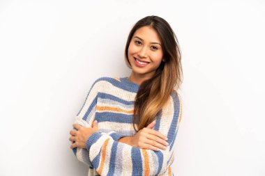 Asyalı güzel bir kadın kollarını kavuşturup mutlu bir şekilde gülüyor, rahat, pozitif ve tatmin edici bir pozla.