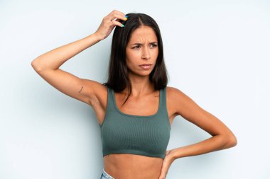 İspanyol güzel kadın şaşkın ve şaşkın hissediyor, başını kaşıyor ve yana bakıyor.