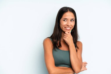 İspanyol güzel bir kadın mutlu, kendinden emin bir ifadeyle gülümsüyor. Elleri çenesinde, merak ediyor ve yan tarafa bakıyor.