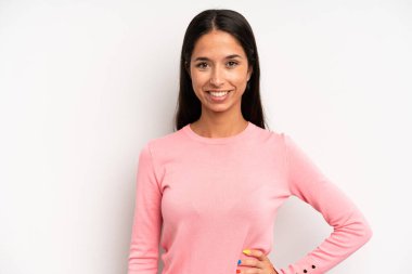 İspanyol güzel kadın mutlu bir şekilde gülümsüyor, eli kalçasında ve kendinden emin, olumlu, gururlu ve arkadaş canlısı.