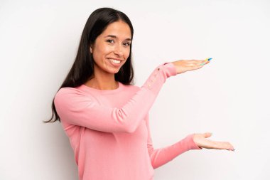 İspanyol güzel kadın gülümsüyor, mutlu, pozitif ve tatmin olmuş hissediyor, fotokopi alanında nesne ya da konsept tutuyor ya da gösteriyor