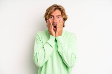 Sarışın, yetişkin bir adam şok olmuş ve korkmuş hissediyor, ağzı açık ve elleri yanaklarında korkmuş görünüyor.