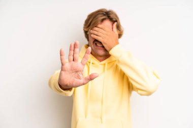 Sarışın, yetişkin bir adam yüzünü eliyle kapatıyor ve kamerayı durdurmak için diğer elini öne koyuyor. Fotoğrafları ve resimleri reddediyor.