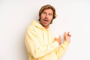 Sarışın, yetişkin bir adam şaşkın ve şaşırmış hissediyor. Yandaki fotokopi alanını işaret ediyor. Şaşırmış ve ağzı açık bakıyor.