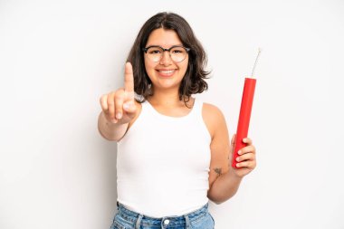 hispanic pretty girl smiling and looking friendly, showing number one. dynamite concept
