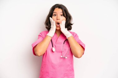 hispanic pretty girl looking surprised and shocked, with jaw dropped holding an object. nurse concept